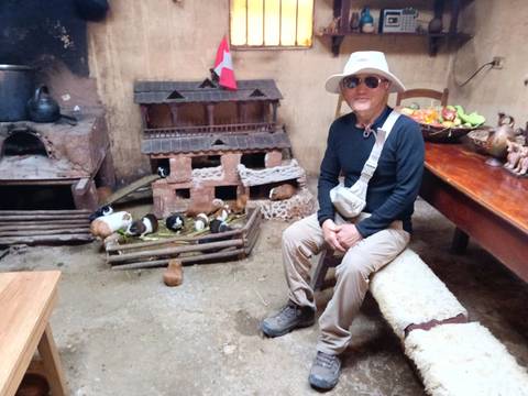       Traveler sits inside a traditional Andean kitchen with guinea pigs in low wooden pens by a clay oven.
  