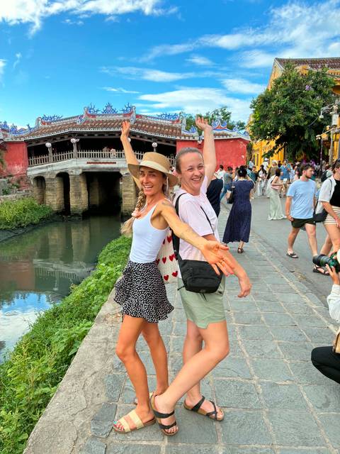       Two women joyfully posing beside the historic Japanese Covered Bridge over a canal.
  