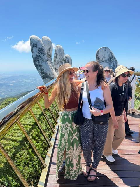       Two women laughing on the famous Golden Bridge with giant stone hands overlooking lush mountains.
  