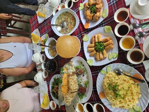       Vietnamese feast spread on a checkered table with fish, spring rolls and soups while diners sit around.
  