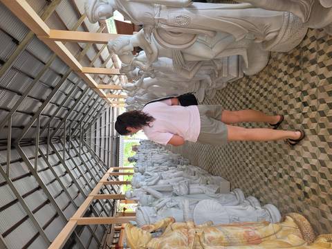       Visitor walking through a workshop lined with white marble statues under a metal roof.
  