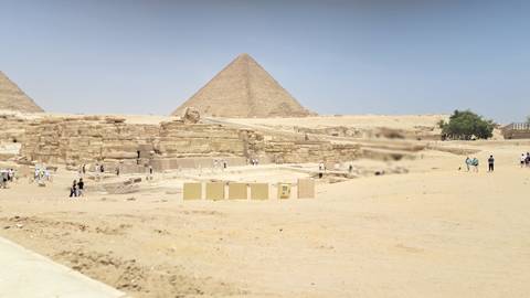       Desert panorama of the Great Pyramid of Giza with tourists exploring the foreground ruins.
  