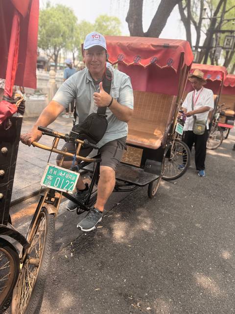       Tourist pedaling a cycle rickshaw along a shaded city street in China.
  