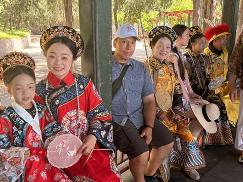       Group of tourists posing with performers in colorful traditional Chinese costumes.
  