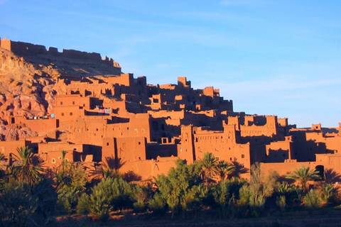       Sun-bathed earthen citadel of Ait Benhaddou contrasts with a clear blue Moroccan sky.
  