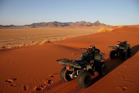       Two quad bikes parked on red desert sands with rugged mountains on the horizon.
  