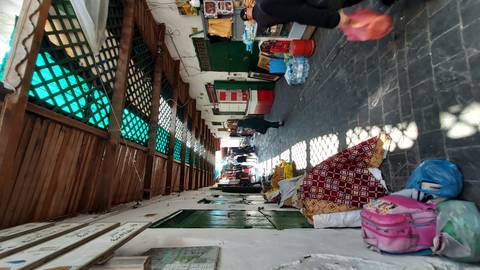       Narrow covered alley of a Moroccan medina lined with shops, goods and locals walking on stone pavement.
  