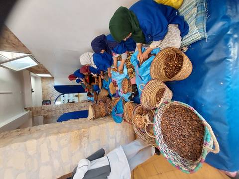       Women in a cooperative seated on the floor cracking argan nuts and sorting them into baskets.
  
