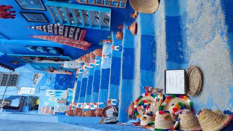       Bright blue staircase in Chefchaouen lined with colorful crafts, ceramics and textiles on display.
  