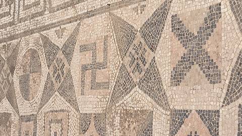      Detail of an ancient mosaic floor with geometric patterns and symbols made of small stone tiles.
  