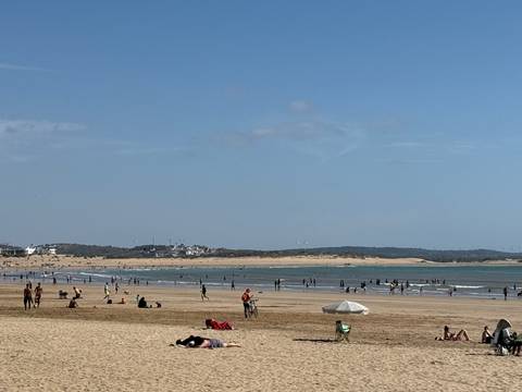       Wide sandy beach with swimmers, kite surfers and sunbathers along a calm Atlantic shoreline.
  