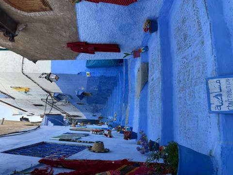       Narrow blue-painted lane in Chefchaouen decorated with flowers and handicrafts.
  