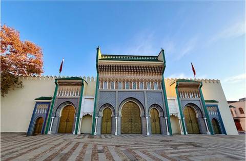       Triple-arched golden gates of the Royal Palace in Fes framed by colorful zellij tiles.
  