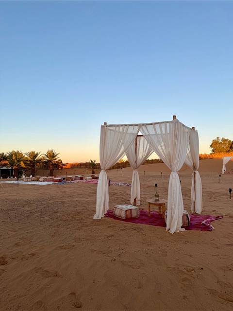       Desert lounge area with white draped canopy and low tables set for relaxation at twilight.
  