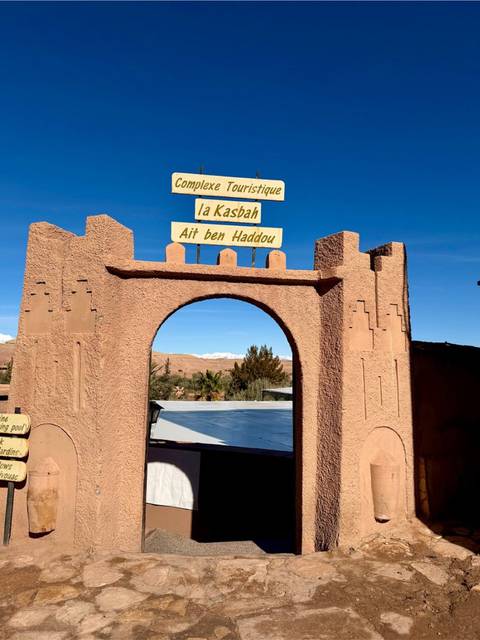       Arched adobe gateway announcing Kasbah Ait Ben Haddou against clear blue sky.
  