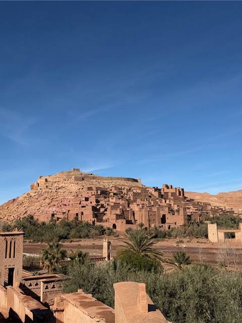      Clay-brick ksar of Ait Benhaddou crowned by a fortress under a deep blue sky.
  