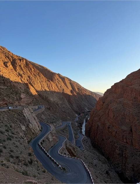       Steep winding road carved into a dramatic rocky gorge lit by late afternoon light
  