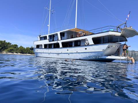       Medium-sized cruise yacht anchored in clear blue water with a swimmer nearby on a sunny day.
  