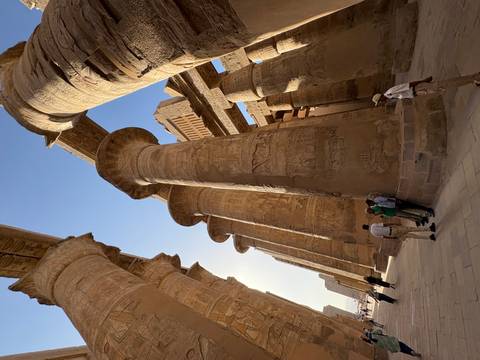      Towering sandstone columns at Karnak with a guide and tourists dwarfed beneath the massive structures.
  