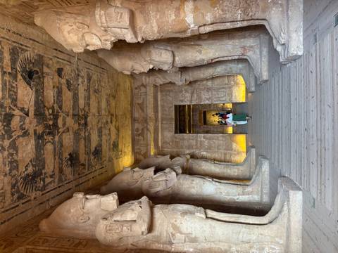       Interior hall of Abu Simbel with colossal standing statues flanking a narrow passage as visitors walk through.
  
