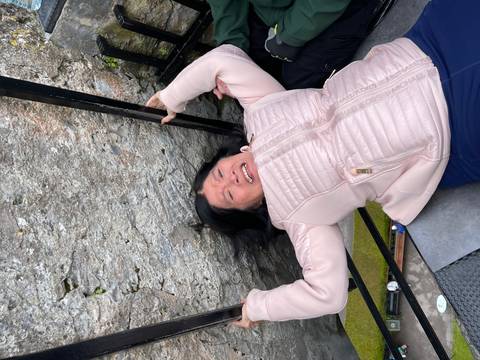       Woman leans backward to kiss the famous stone set into a castle wall, gripping side rails for support.
  