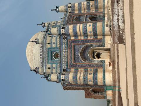       Magnificent blue-and-cream striped mausoleum with ornate tile work and a large domed roof set against a pale sky.
  