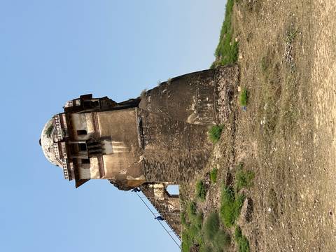       Weather-worn stone watchtower rising above grassy earthworks, remnants of an old fort under clear skies.
  