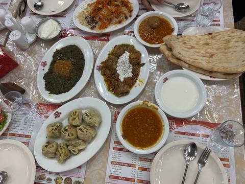       Overhead shot of a Pakistani meal featuring dumplings, stews, yogurt and naan bread laid out on a restaurant table.
  