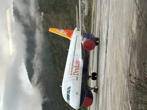       Royal Bhutan Airlines (Drukair) Airbus parked on Paro airport apron with misty forested hills behind.
  