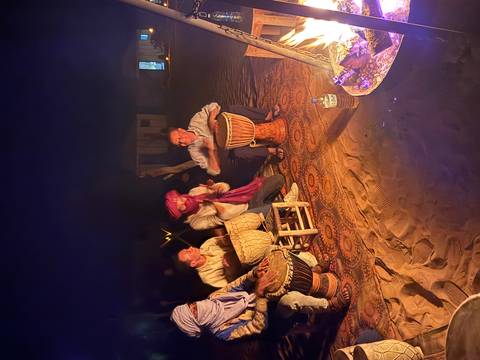       Musicians and travellers drumming around a campfire on desert sand under the night sky
  