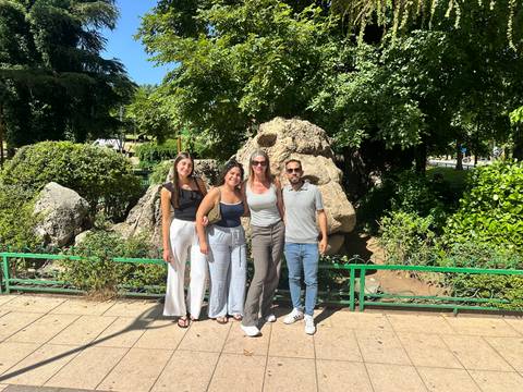       Four smiling travellers posing together in a sunny park with lush green foliage.
  