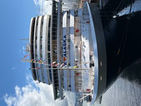       Large Holland America cruise ship docked with a banner reading 'I ♥ ALASKA' under blue sky.
  