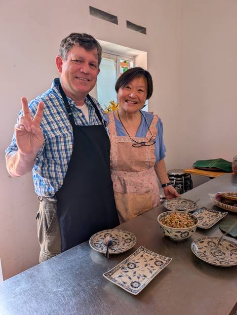       A smiling couple in aprons present a freshly prepared Vietnamese dish during a cooking class.
  