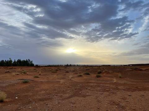       Vast reddish desert plain under dramatic cloudy sky with sun breaking through
  