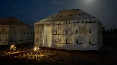       Desert campsite at night with canvas tent illuminated by lantern light under starry sky
  