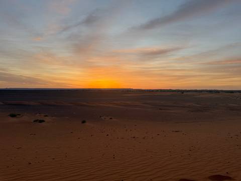       Fiery orange sunset over a flat desert plain with pastel clouds streaking the sky.
  