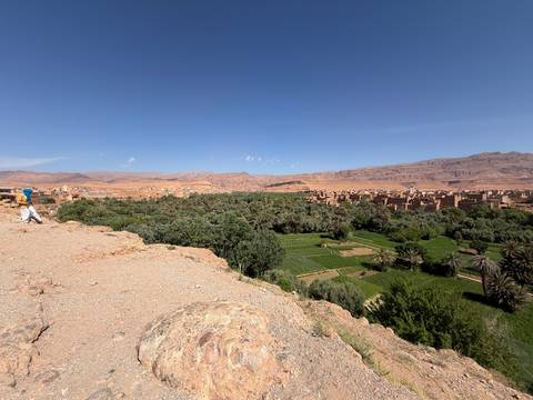       Panoramic view over a lush oasis valley with adobe village and mountains beyond.
  