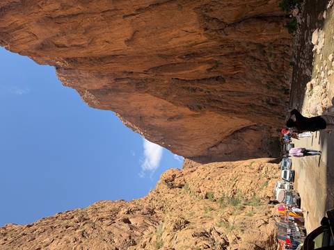      Towering orange cliffs of Todra Gorge with tourists and vehicles passing below.
  