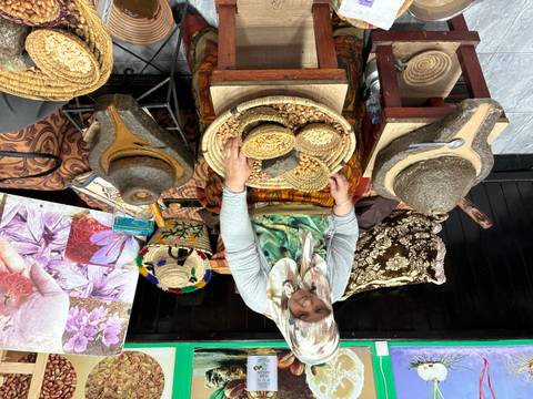       Woman in headscarf processing nuts with traditional stone grinders and woven baskets in a Moroccan market
  