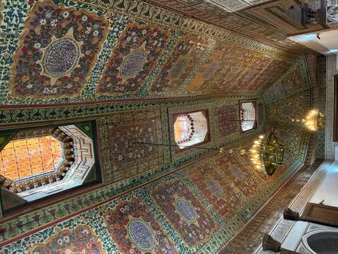       Intricately painted and carved wooden ceiling with ornate chandeliers in a Moroccan palace
  