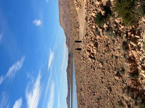       Two distant figures walk along a rocky lakeside plain beneath a bright blue sky.
  