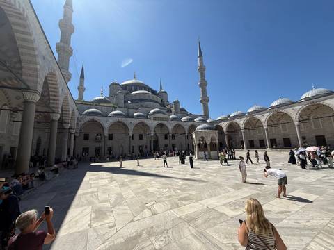       Courtyard of Istanbul’s Blue Mosque with worshippers and visitors under clear blue sky.
  