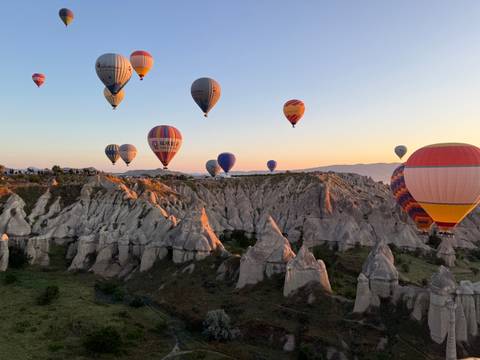       Multiple colorful hot-air balloons float over sun-lit fairy chimneys at golden hour in Cappadocia.
  