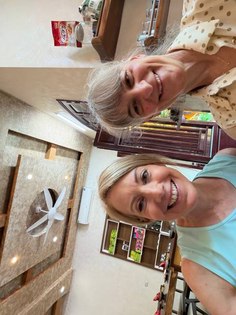      Close selfie of two happy women inside a stylish, light-filled interior.
  