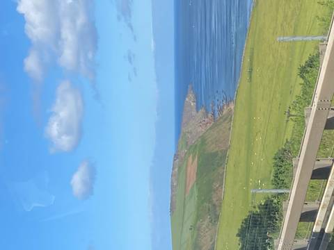       Green coastal cliffs meeting a blue sea under scattered clouds.
  