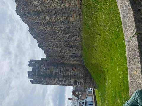       Stone defensive wall and round tower of Caernarfon Castle under grey sky.
  