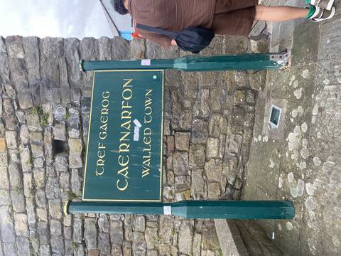       Green sign marking Caernarfon Walled Town attached to stone wall.
  