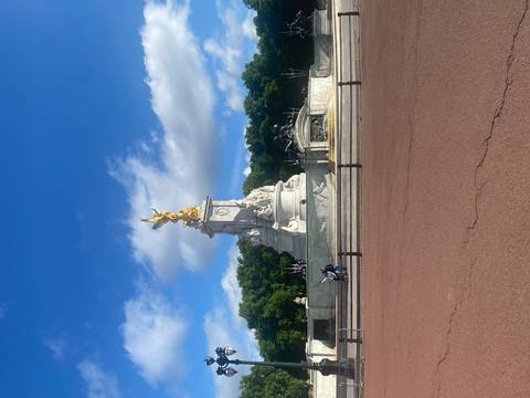       Victoria Memorial with gilded angel in front of Buckingham Palace under blue sky.
  