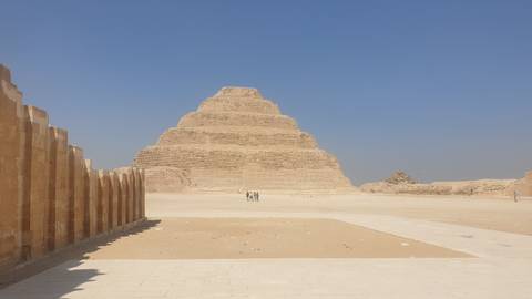       Wide shot of the Step Pyramid of Djoser rising from the sandy desert plateau under a clear blue sky.
  