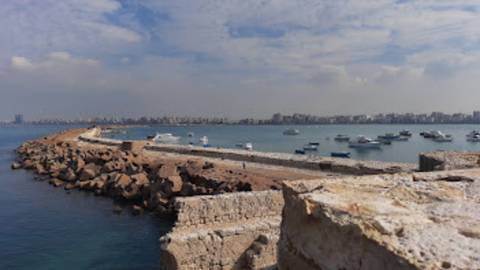       Blurry coastal breakwater with moored boats and distant skyline under hazy skies.
  